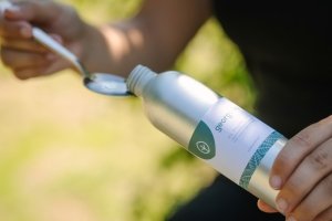 Georganics Oil Pulling Mundwasser wird in einen Löffel gegossen, bereit zur Anwendung in einer natürlichen Außenumgebung.