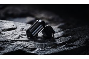 Schwarze Turmalinkristalle auf einem Rohstein unter atmosphärischem Licht, Symbol für Schutz und energetische Erdung.